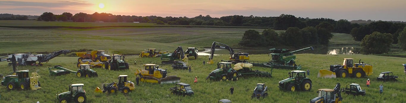 Lidé procházející se mezi několika typy zařízení John Deere na rozsáhlém poli.