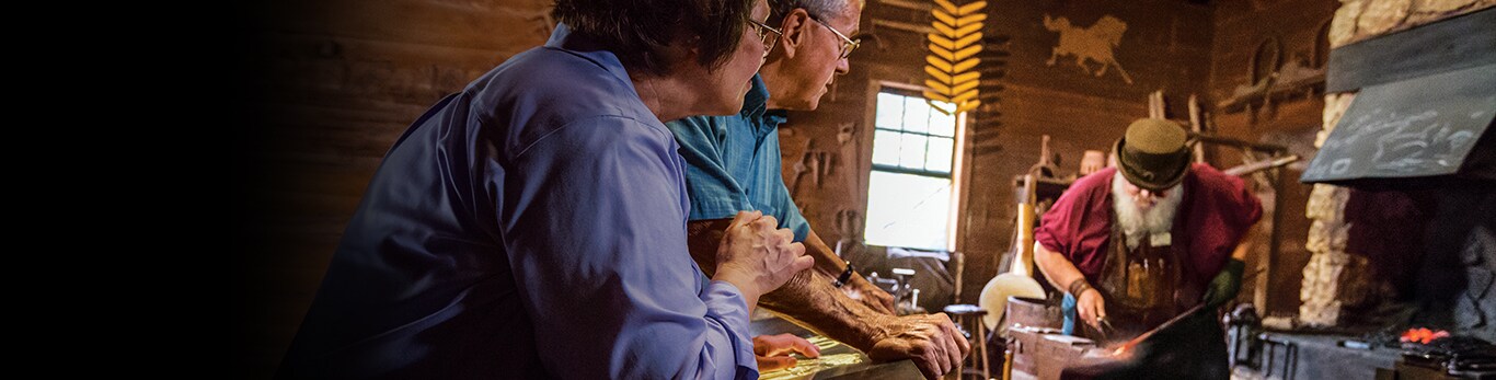 Starší pár pozoruje kováře při výrobě kladiva na historickém místě v Grand Detour, Illinois, Spojené státy americké