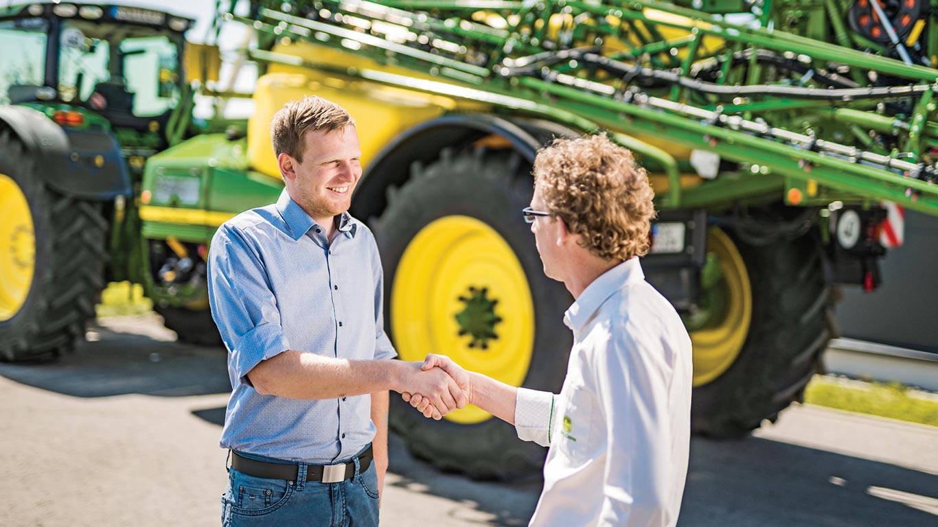 Potřesení rukou prodejce a zákazníka před postřikovačem John Deere