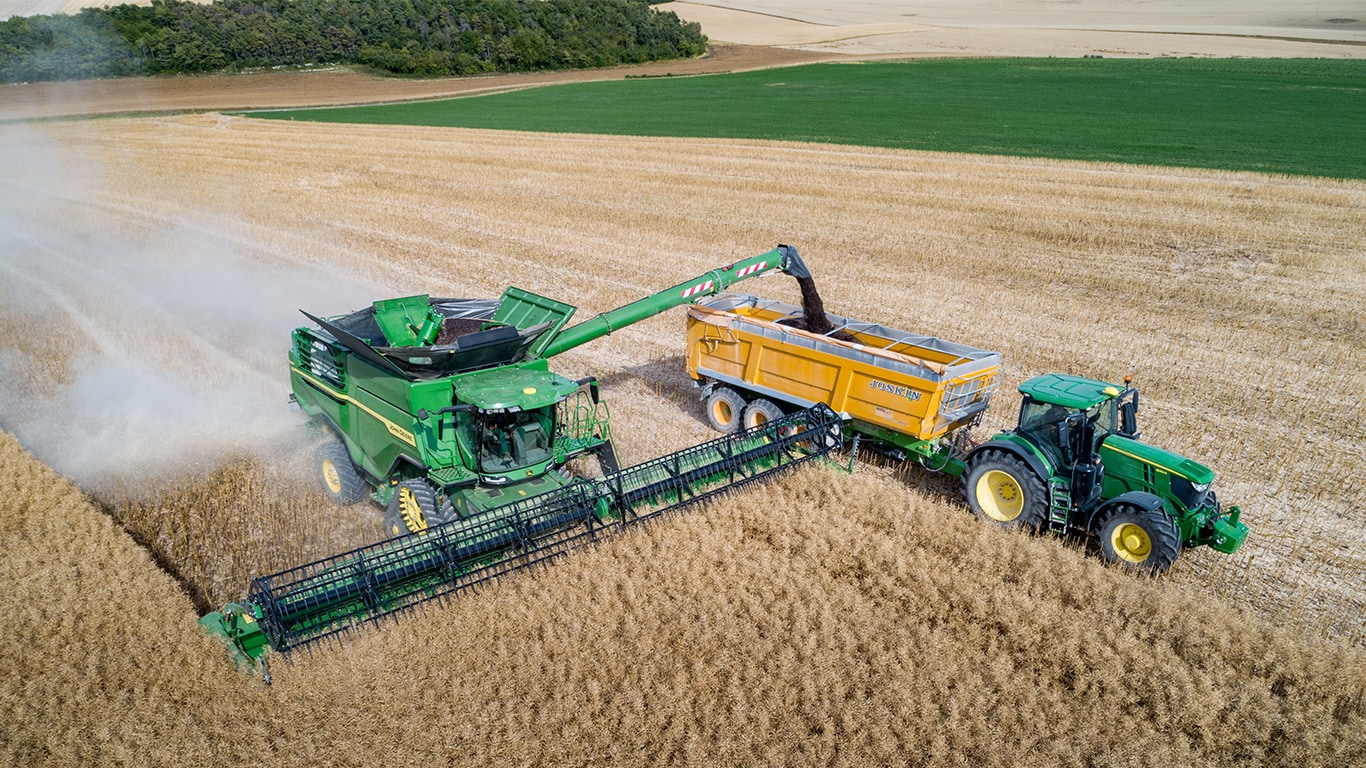 Skl&iacute;zec&iacute; ml&aacute;tička John Deere řady X vykl&aacute;d&aacute; řepkov&eacute; semeno do&nbsp;př&iacute;věsu na&nbsp;zrn&iacute; tažen&eacute;ho traktorem John Deere