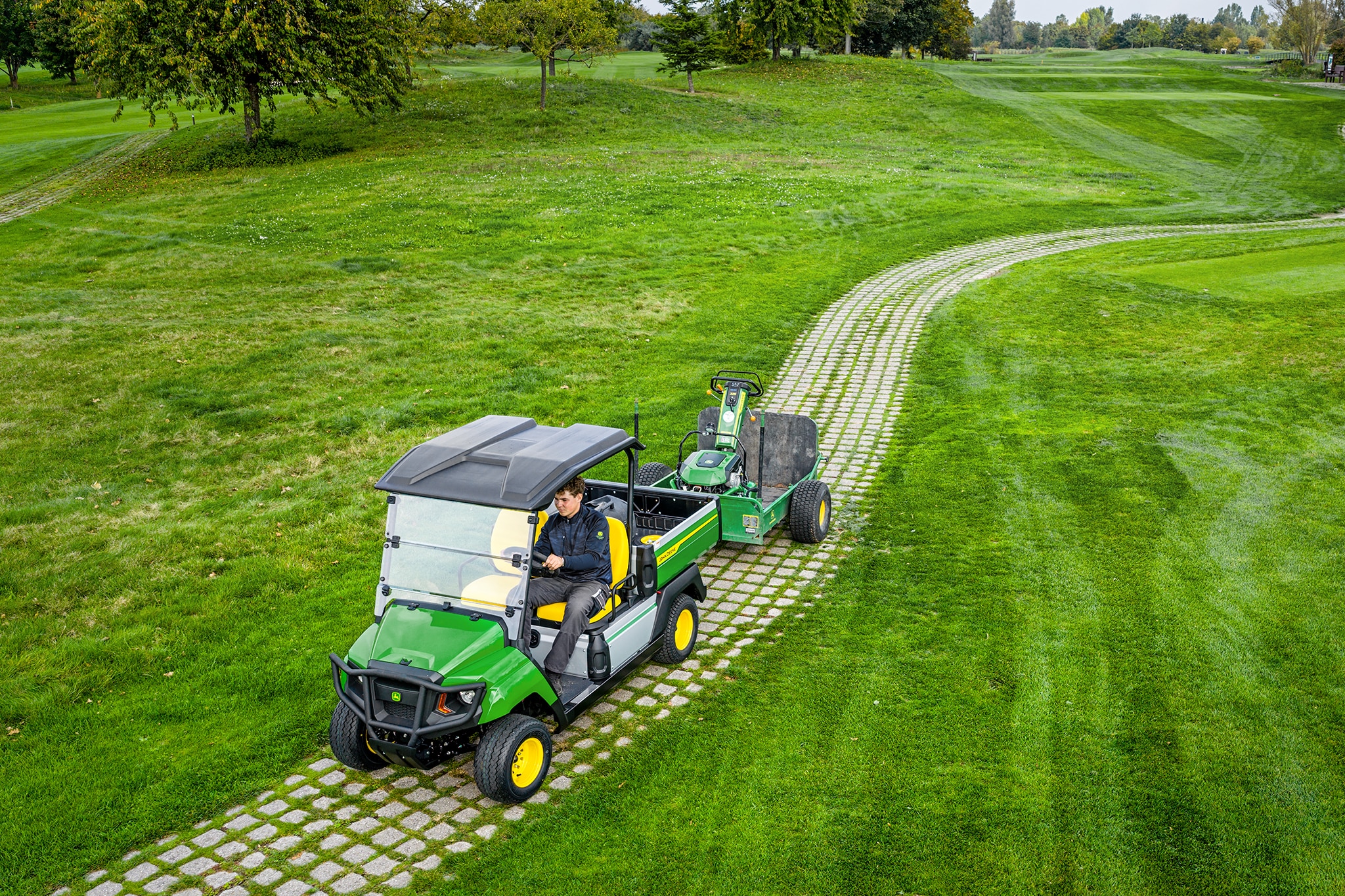Zařízení John Deere Gator GS táhnoucí náklad na travnaté cestě golfového hřiště