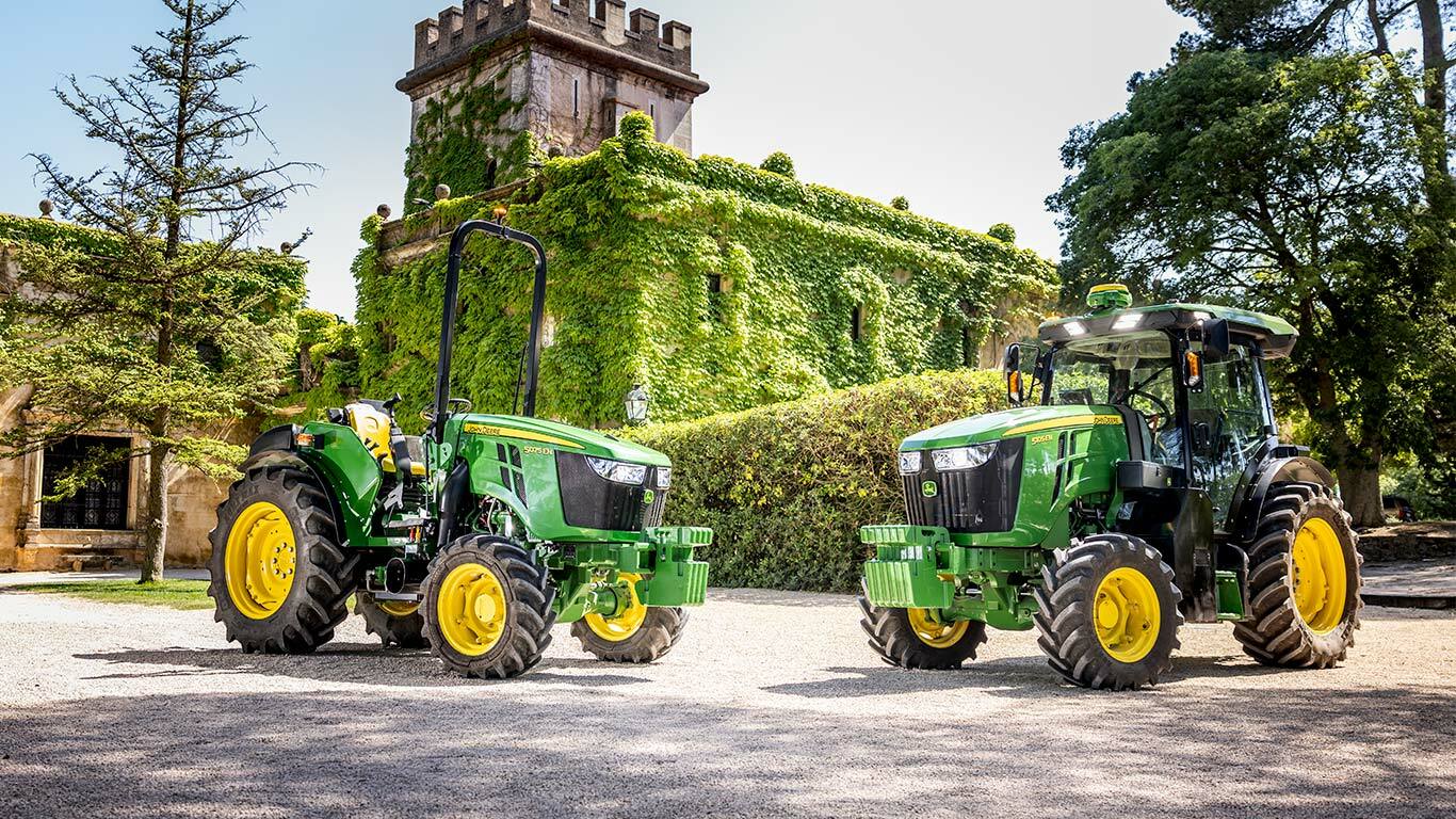 Zelenožlutý traktor John Deere 5075EN projíždí ovocným sadem po polní cestě, obklopený ovocnými stromy a slunečním světlem.