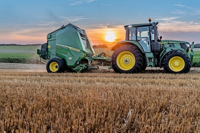 John Deere V462M na slámovém poli tažený strojem John Deere 6M 150 při západu slunce