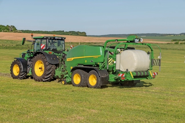 Ovíjecí balíkovač John Deere C442R tažený traktorem John Deere 6R 185 provádí lisování balíků siláže o vysoké hustotě