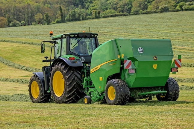 Sběrací lis John Deere F442M tažený traktorem John Deere 6M na kopcovitém travním poli