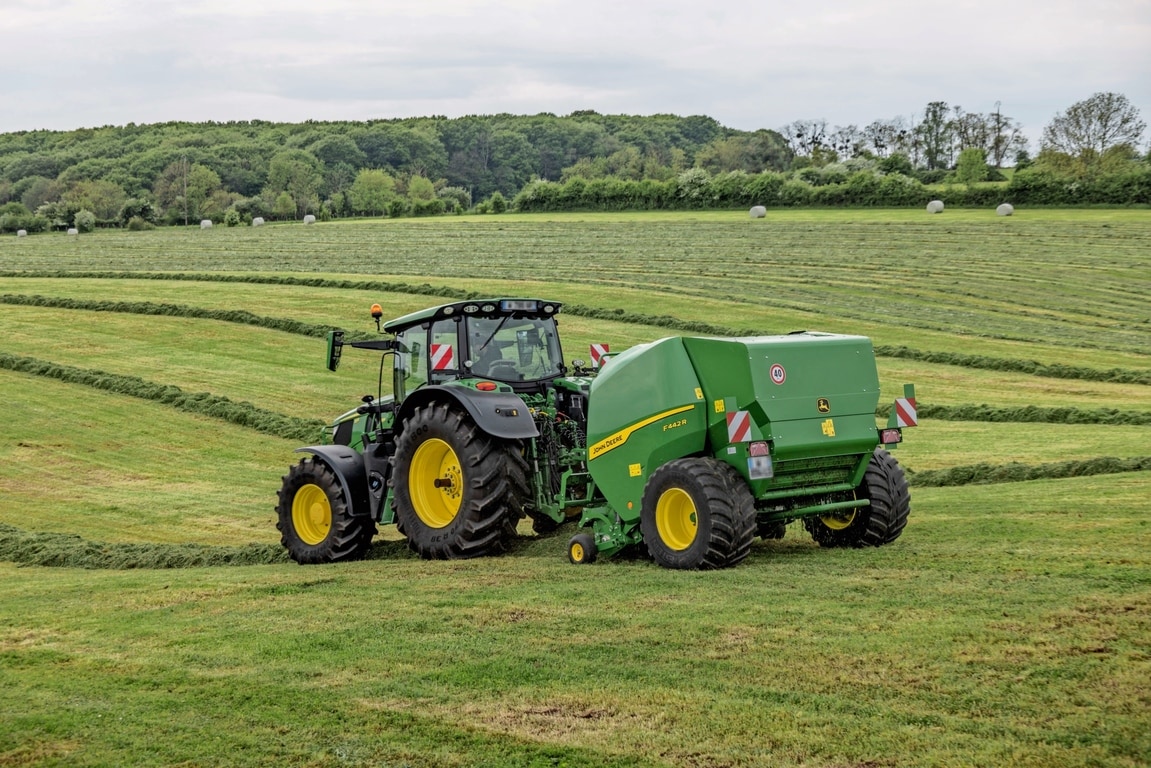 Sběrací lis John Deere F442R tažený traktorem John Deere 6M na kopcovitém travním poli