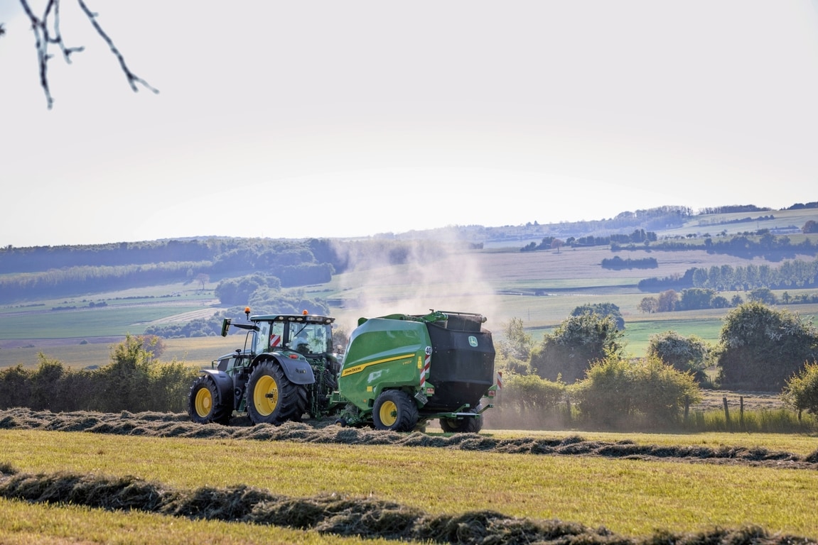John Deere V462R tažený traktorem John Deere 6R 185 při lisování sena