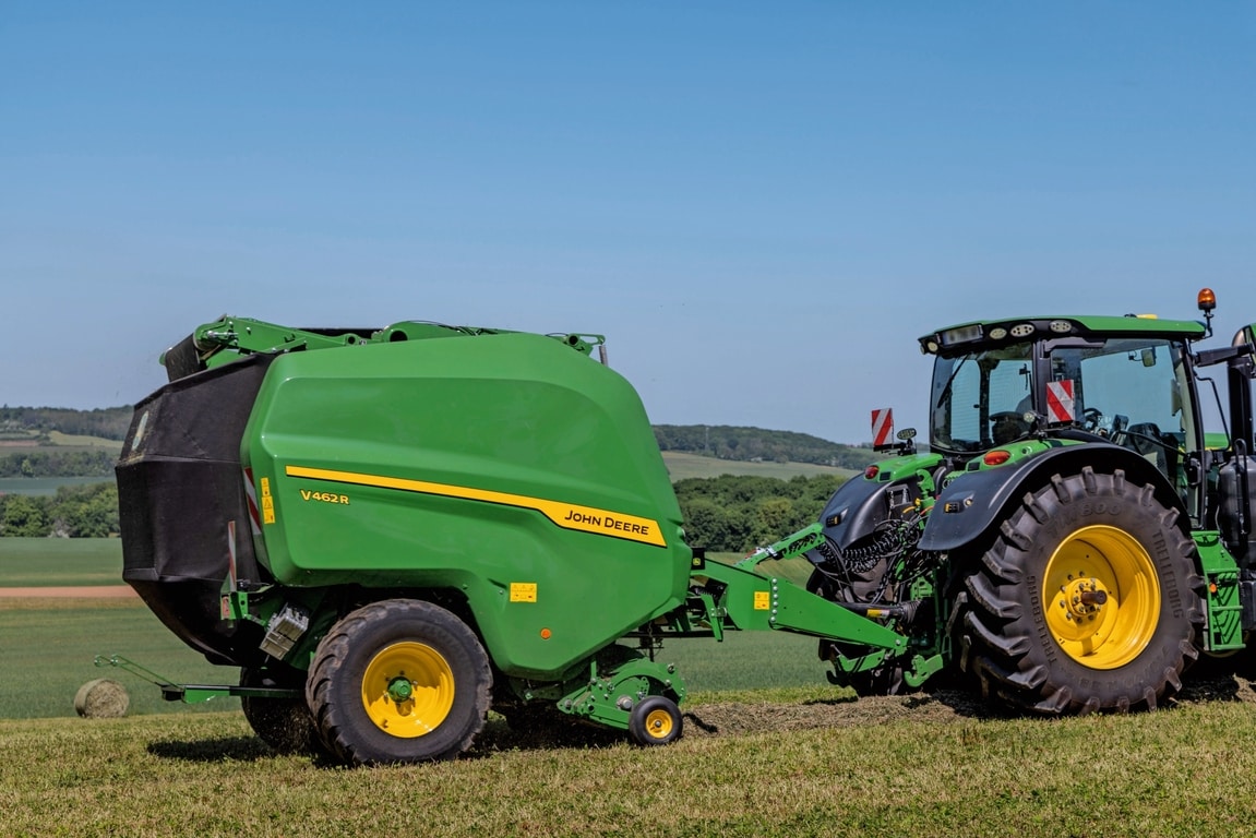 John Deere V462R tažený traktorem John Deere 6R 185 při lisování sena